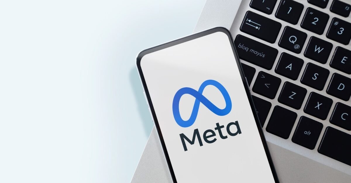 A-smartphone-displaying-the-Meta-logo-rests-on-a-laptop-keyboard-with-a-light-background